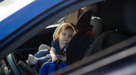 Sad little child girl alone in the car waiting for the parent strapped in a child car seat. It is dangerous to leave children in the car in hot weather.