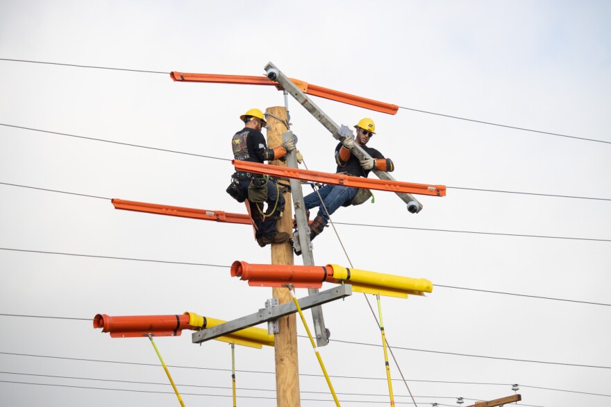 Lineman: Two workers are surrounded by wires near the top of a telephone pole.