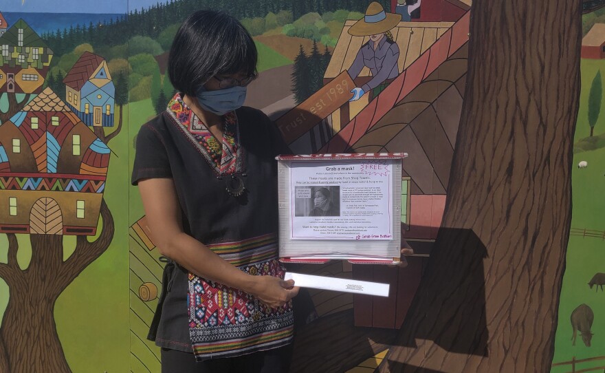 Greacen holds up one of the mask dispensers that she designed. They are made of recycled campaign signs.