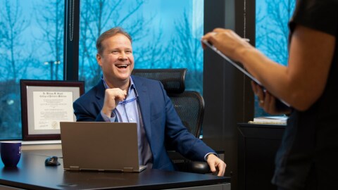 man sitting at desk in medical office laughing