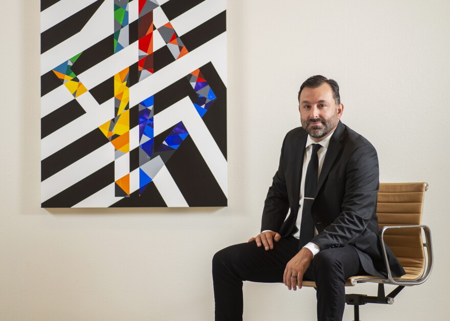 Scott Malbaurn sits beside a geometric painting with black-and-white stripes and colorful triangles.