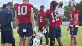 University of Connecticut quarterbacks, Cale Millen, second left, Penn State transfer Ta'Quan Roberson, third left, and Tyler Phommachanh, second from right, gather during the opening day of NCAA college football training camp on July 29, 2022, in Storrs, Conn. Roberson started the season-opening game for UConn, but he was unable to finish it. He suffered a knee injury in a 31-20 loss at Utah State. (AP Photo/Pat Eaton-Robb)