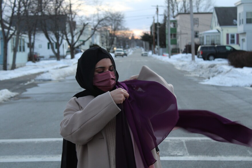 A woman drapes a purple hijab over her shoulder while standing in a residential street. 