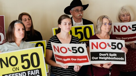People hold up signs opposing Prop 50 during a press conference in Chico, Calif., Wednesday, Oct. 29, 2025.