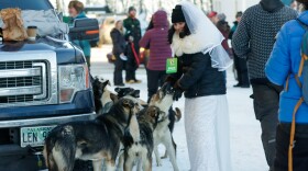A woman with a wedding dress pets a dog.