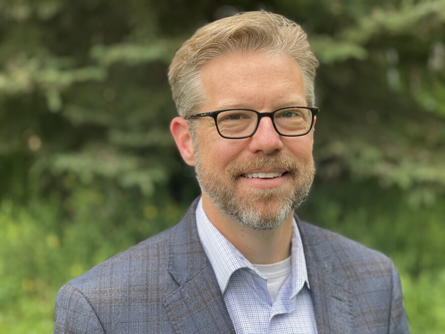 A man wearing glasses and a blazer stands for a portrait photo.