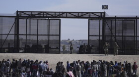 FILE - Migrants who crossed the border from Mexico into the U.S. wait next to the U.S. border wall where U.S. Border Patrol agents stand guard, seen from Ciudad Juarez, Mexico, Thursday, March 30, 2023. The Biden administration will open migration centers in South and Central America for asylum seekers heading to the U.S.-Mexico border, in a bid to slow what’s expected to be a surge of migrants seeking to cross the border next month as pandemic-era immigration restrictions end, U.S. officials said Thursday, April 27. (AP Photo/Fernando Llano, File)