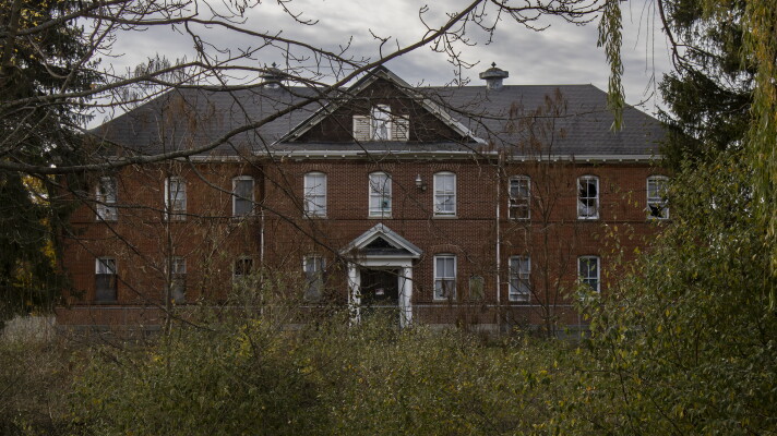 A boarded-up schoolhouse on the campus of the Mount Pleasant Indian Industrial Boarding School. The site is currently closed to the public, with "No Trespassing" signs stationed around the property.