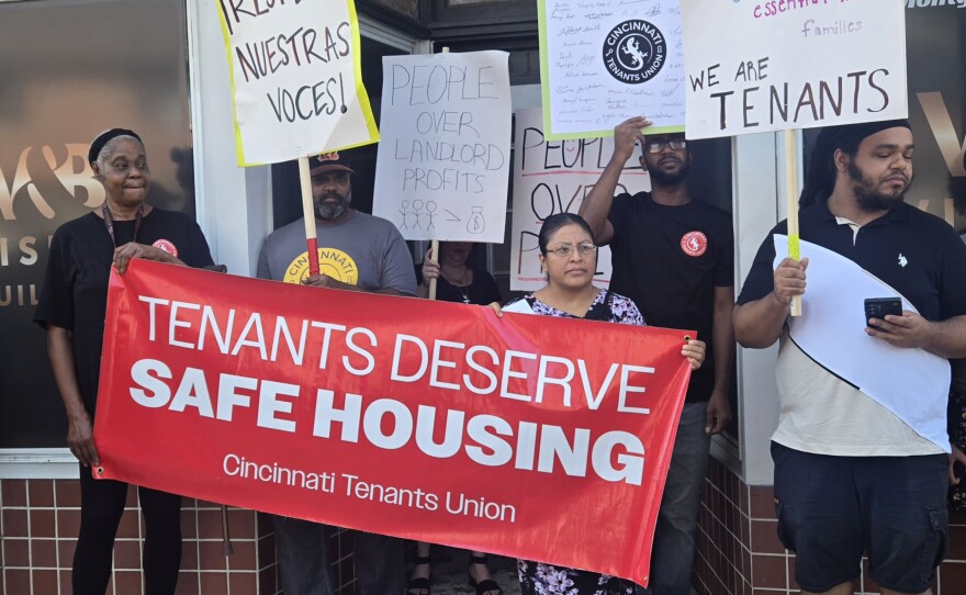 People stand outside an apartment building with signs reading "we are tenants" and "people over landlord profit."