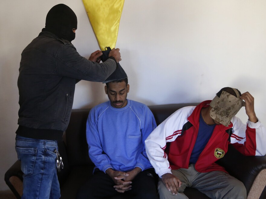 A Kurdish security officer takes face masks off Alexanda Amon Kotey (left) and El Shafee Elsheikh, who were allegedly among four British jihadis who made up a brutal Islamic State cell dubbed "The Beatles," for an interview at a security center in Kobani, Syria, last year.