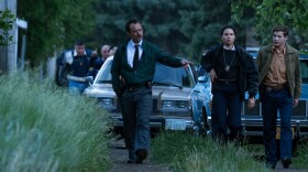 Actors Jude Law, Jurnee Smollett, and Tye Sheridan walk in front of two parked cars as they portray FBI field agents in the new movie 'The Order.'