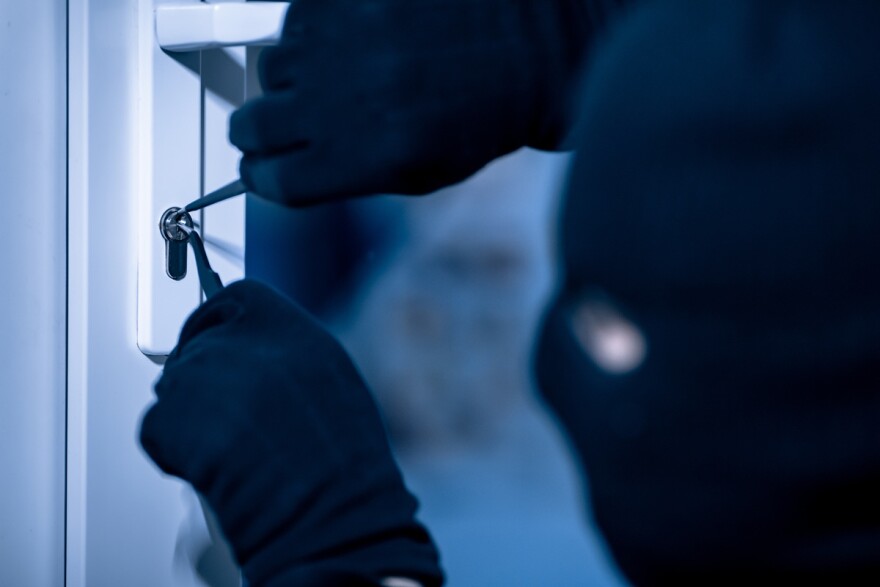 Closeup of gloved robber in a black mask cracking a door lock with metal picklock tool 