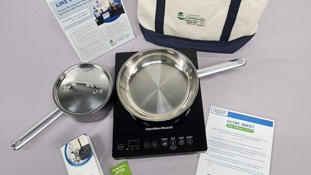 Items from a cooking kit - including a silver pot, pan, and a black induction cooker - arranged as a display