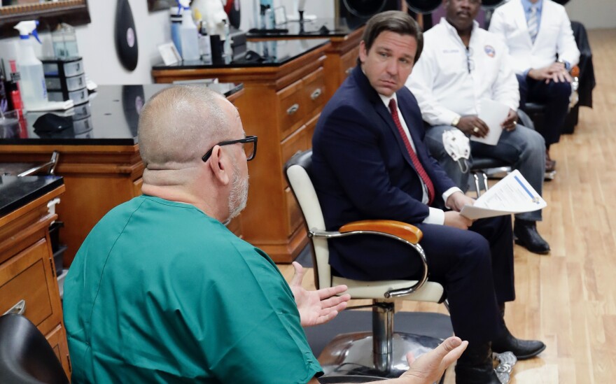 Dr. Raul Pino, left, Director of Florida Department of Health in Orange County speaks to Florida Gov. Ron DeSantis, during a discussion about opening businesses such as barber shops and nail and hair salons during at a news conference Saturday, May 2, 2020, in Orlando, Fla. (AP Photo/John Raoux)