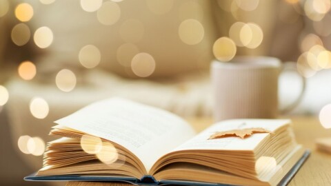 Open book on table with glowing light spots all around and mug in background
