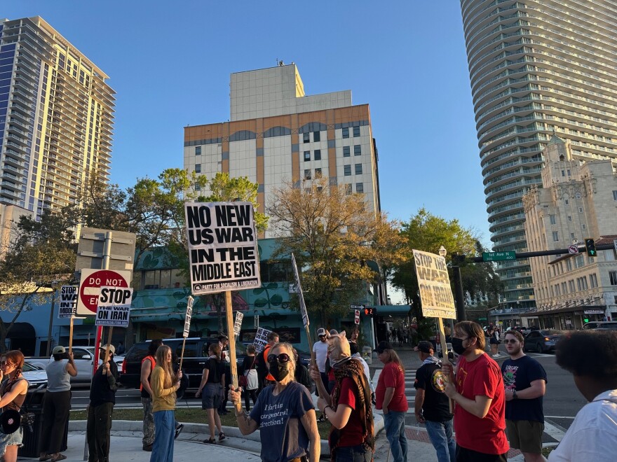 people holding protest signs, some wearing masks, gathered on the intersection of 3rd street and first avenue of downtown St. Petersburg
