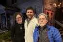 Three people stand on a sidewalk in the evening.