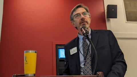 A man wearing a dark blue suit stands behind a podium and looks into the distance.