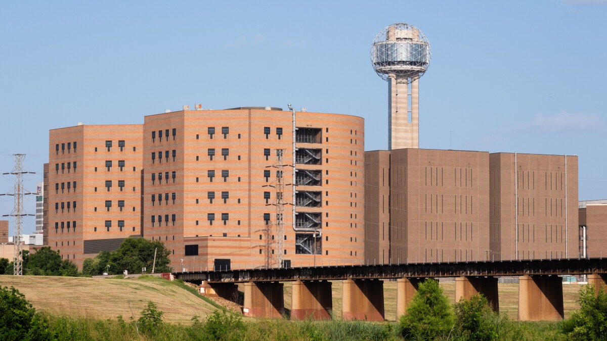 A large brick building is seen behind a river trail.