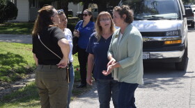 Four women standing next to each other in a semi circle on a residential street and in front of a white van.