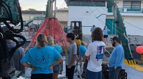 About nine people standing on or near the boat about to depart wearing blue and white shirts.