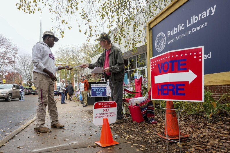 Stephen McCutcheon, right, gives a sample Republican ballot to Douglas Frick outside the West Asheville Public Library on Election Day, Tuesday, Nov. 5, 2024 in Asheville, N.C.