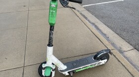 A Lime scooter on a sidewalk next to car street parking.