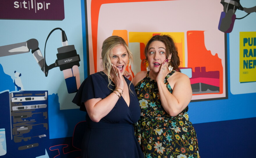 Two guests at the 2026 Hear the Future gala pose in a photo booth with their hands on their cheeks. The booth is painted to resemble the Saint Louis Public Radio studio, but with a whimsical display of colors.