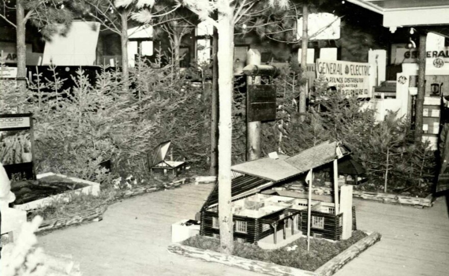 Display of a miniature house at the Black Hills Industrial Show. Fish & Hunter Co. pictured in the background. Date: 1935.