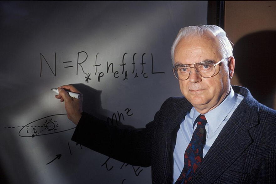 Frank Drake poses in front of white board with the Drake Equation