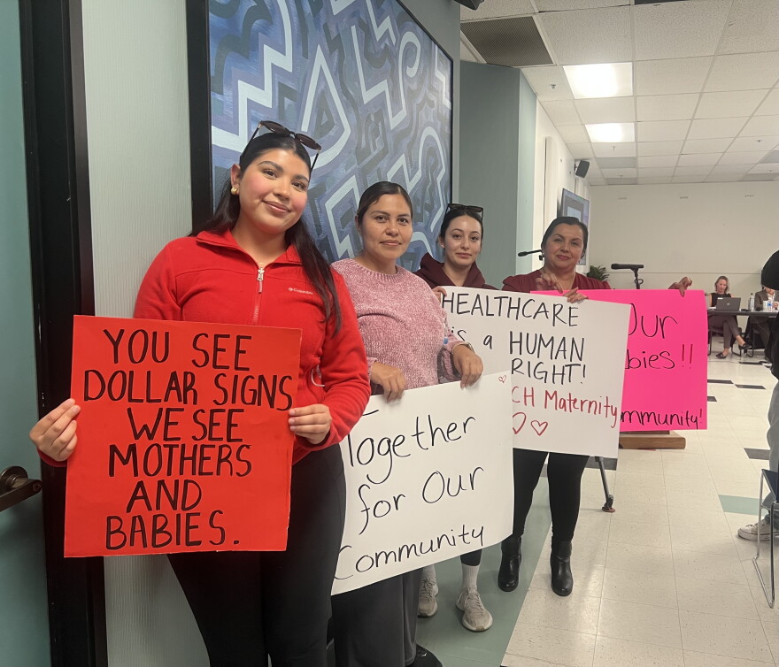 People stand along a wall with signs held out in front of them.