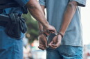 a police office handcuffs a man, the man has his hands cuffed behind his back