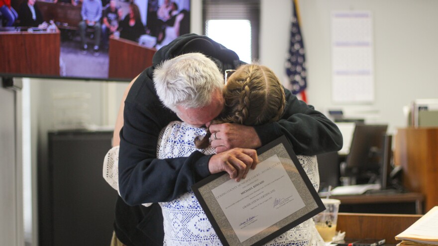 A man hugs a woman. He holds a certificate in his hand that says, "Licking County Municipal Court - H.O.M.E. Court - this certifies that Michael Kincaid has successfully completed the Licking County Municipal Court - H.O.M.E. Court Program and is there awarded the graduate certificate." 