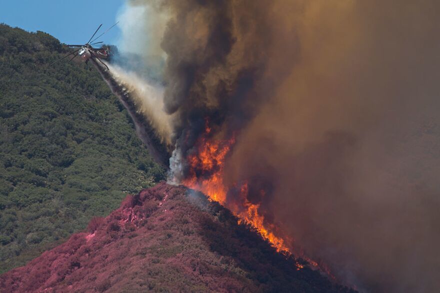 A firefighting helicopter pilot tries to stop flames close to jumping a ridge above Cajon Boulevard at the Blue Cut Fire on Thursday near Wrightwood, California.