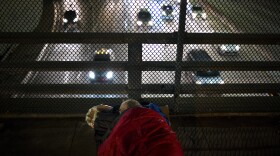 A homeless man lies tucked in a sleeping bag on an overpass above the Freeway.