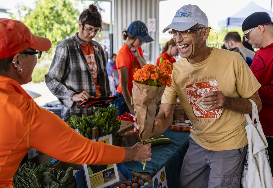 Liz Graznak (CQ), owner of Happy Hallow Farm, hands Daniel Kuebler (CQ) a bouquet of flowers after paying for vegetables on Aug. 29, 2026, in Columbia. Graznak gave the first one hundred customers a free bouquet with their purchase and the flowers were seen carried up and down Columbia Farmers Market.