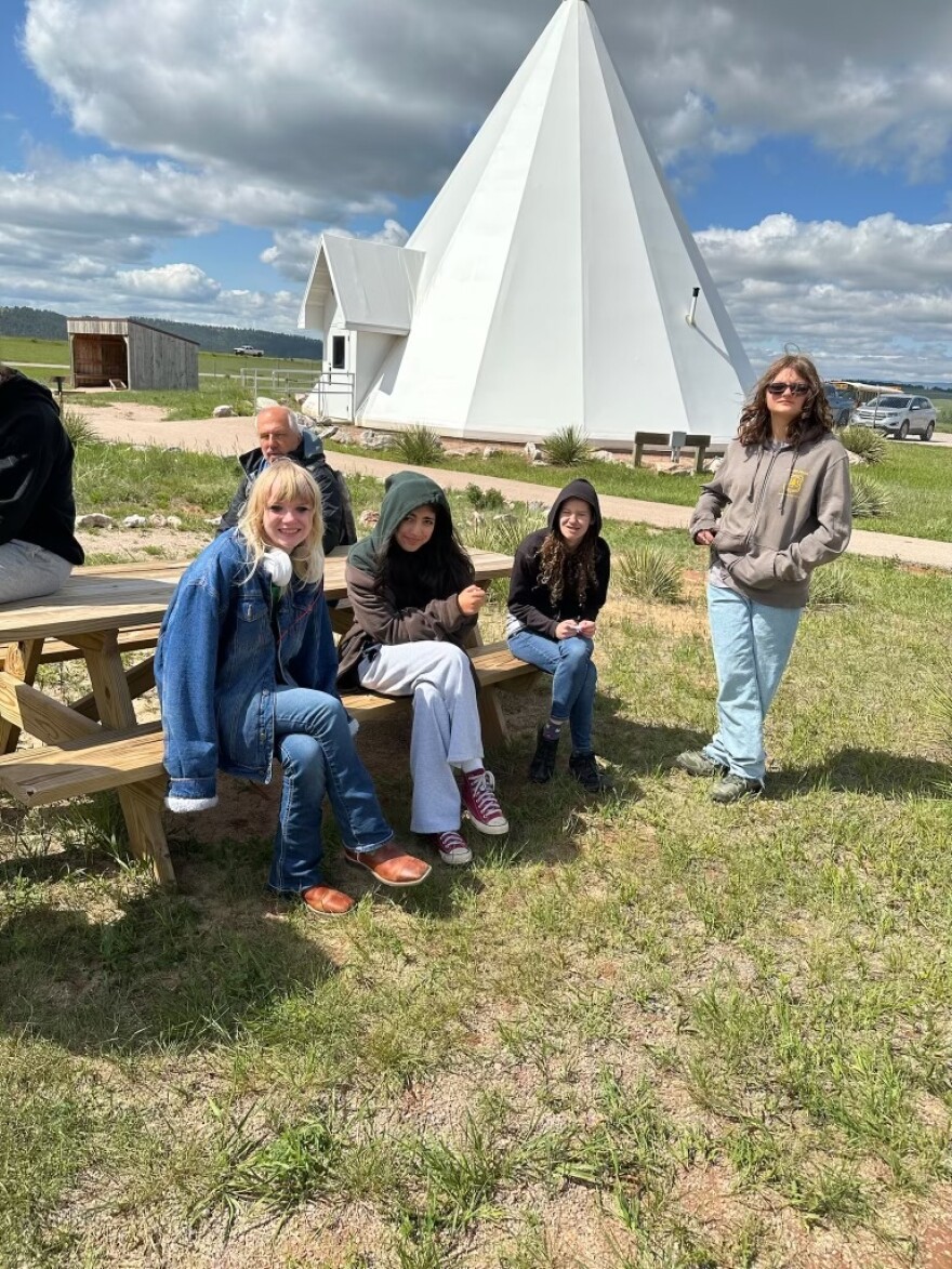 Three kids and a couple of adults in front of a building shaped like a teepee