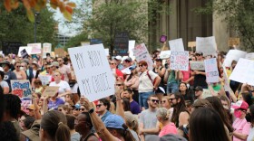 a crowd of people gather in front of the Indiana Statehouse. Some hold signs. The signs read: "My Body My Choice", "Abortion on demand and without apology" and "Protect Women's Rights"