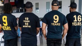 Members of the Organization of Exonerees wear t-shirts displaying the exact number of years they spent wrongfully incarcerated for crimes they did not commit. All the t-shorts are black and the numbers are on the back. The far left on says 9 years. The one next to it says 19 years and 10 months. The next one also says 9 years and the last says 16 years. 