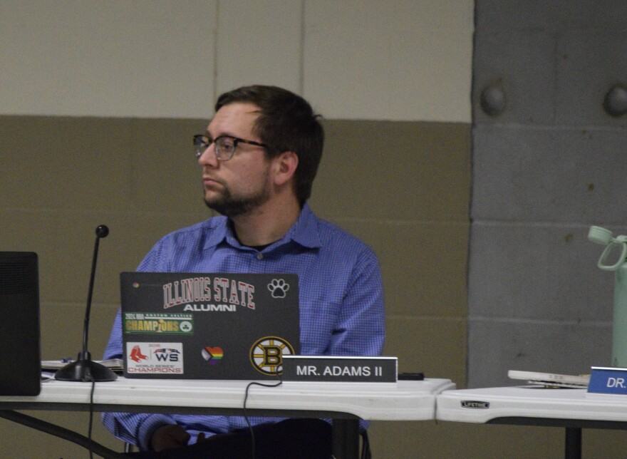 Man with glasses in blue shirt watches as someone else is speaking.