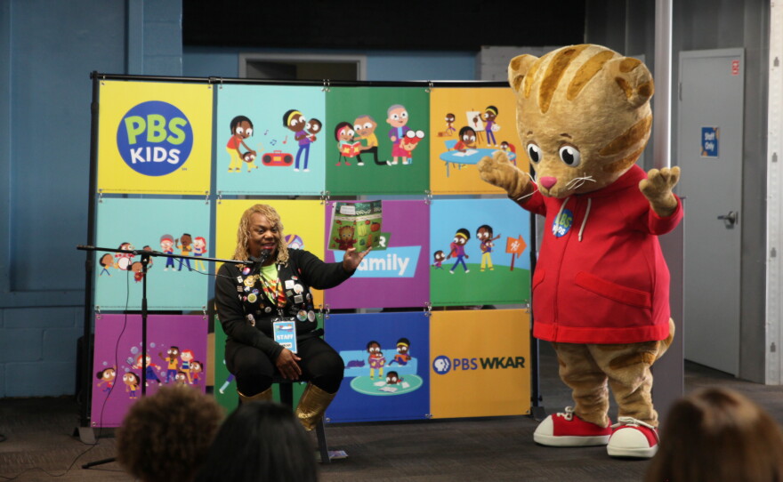 Woman holding up book as she reads, with Daniel Tiger costume character