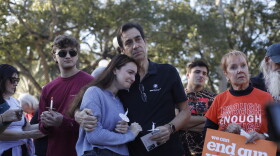 A young woman cries on her fathers shoulder and holds a candle. Others stand around holding signs to "end gun violence."