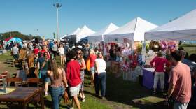 A crowd of people shop at white pop up tents outside. 