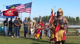 Men at powwow, dancing or holding flags. 