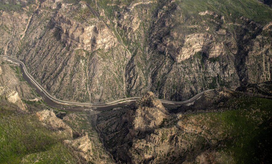 An overhead shot of an interstate, from way up high. The interstate is a ribbon weaving through the middle of a deep, rugged, rocky canyon.