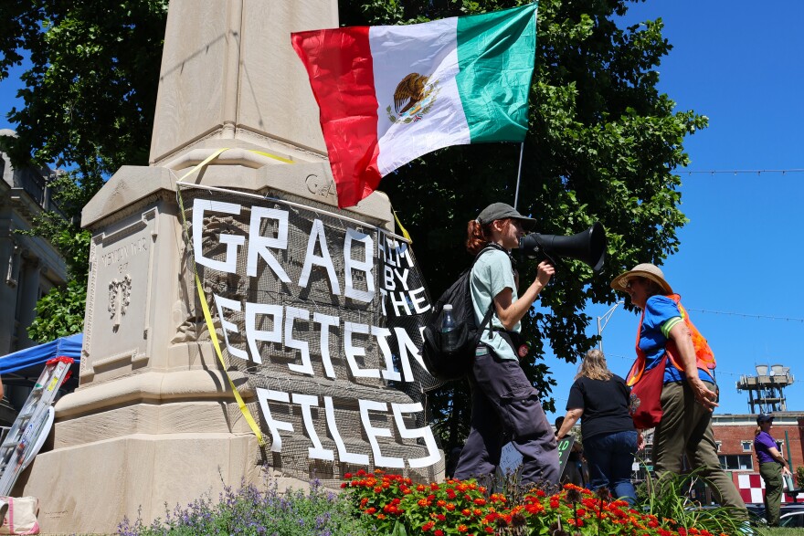 After marching to Indiana University's Sample Gates, a demonstrator holds a Mexican flag in front of a banner that reads, "Grab him by the Epstein files." Another sign read, "Trump is traitor."