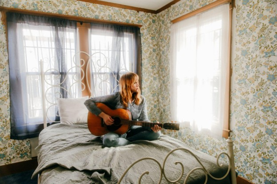 Flock of Dimes' Jenn Wasner playing the guitar on a bed