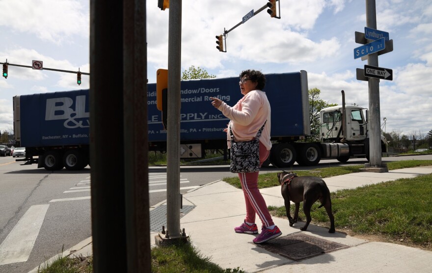 Nancy Hernandez Maciuska, a member of the Lewis Street Committee, walks her dog, Hope, along Scio Street as trucks pull off the Inner Loop exit onto Lyndhurst Street. Of the city's talk to fill in the Inner Loop, she says, 'We want to be heard.'