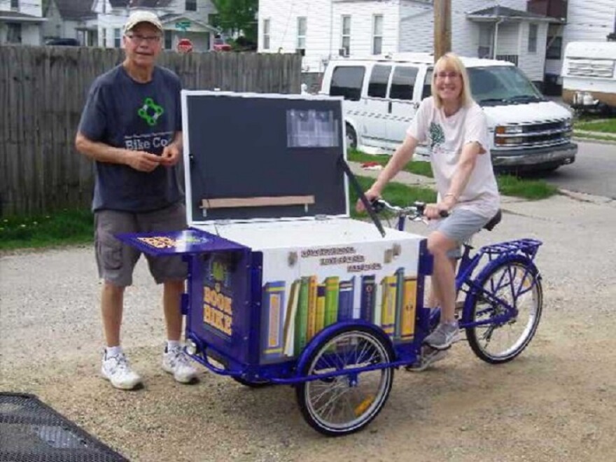 Woman on bicycle holding box of books