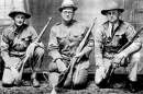 Three World War I era soldiers or rifle team members kneeling in uniform, holding bolt-action rifles, with a trophy placed on the floor in front of them.